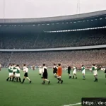 축구 전술 변화와 역사 - A dynamic 1950s football match scene showing two teams in vintage kits on a grass pitch under a clou...